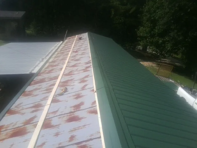Old rusted panels beside newly installed green metal roofing — Wind Damage Roof Repair by Roofing Brothers in East Springfield