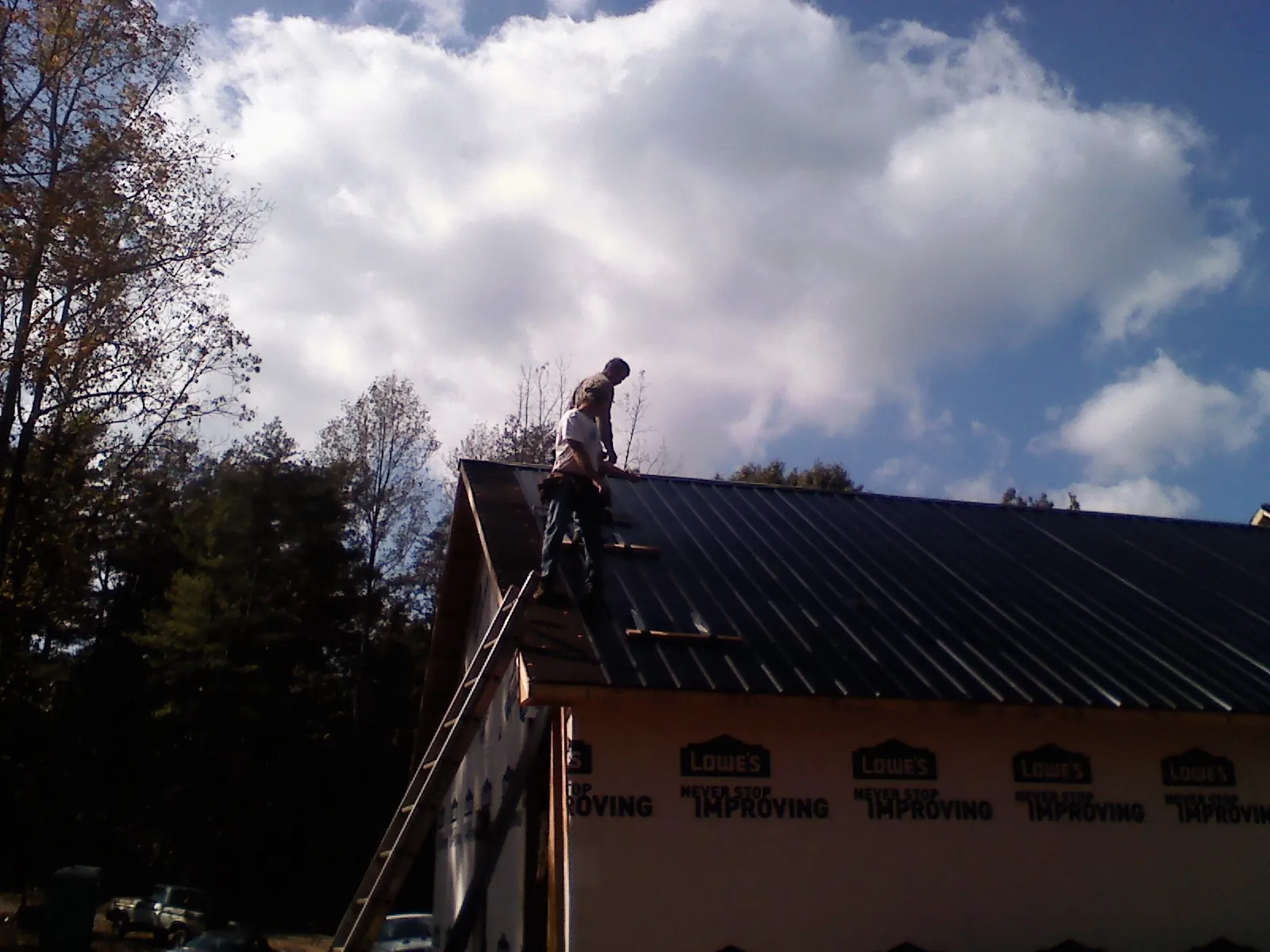 Roofer fastening dark metal panels high against a cloudy sky, from a Roof Inspection job in East Springfield