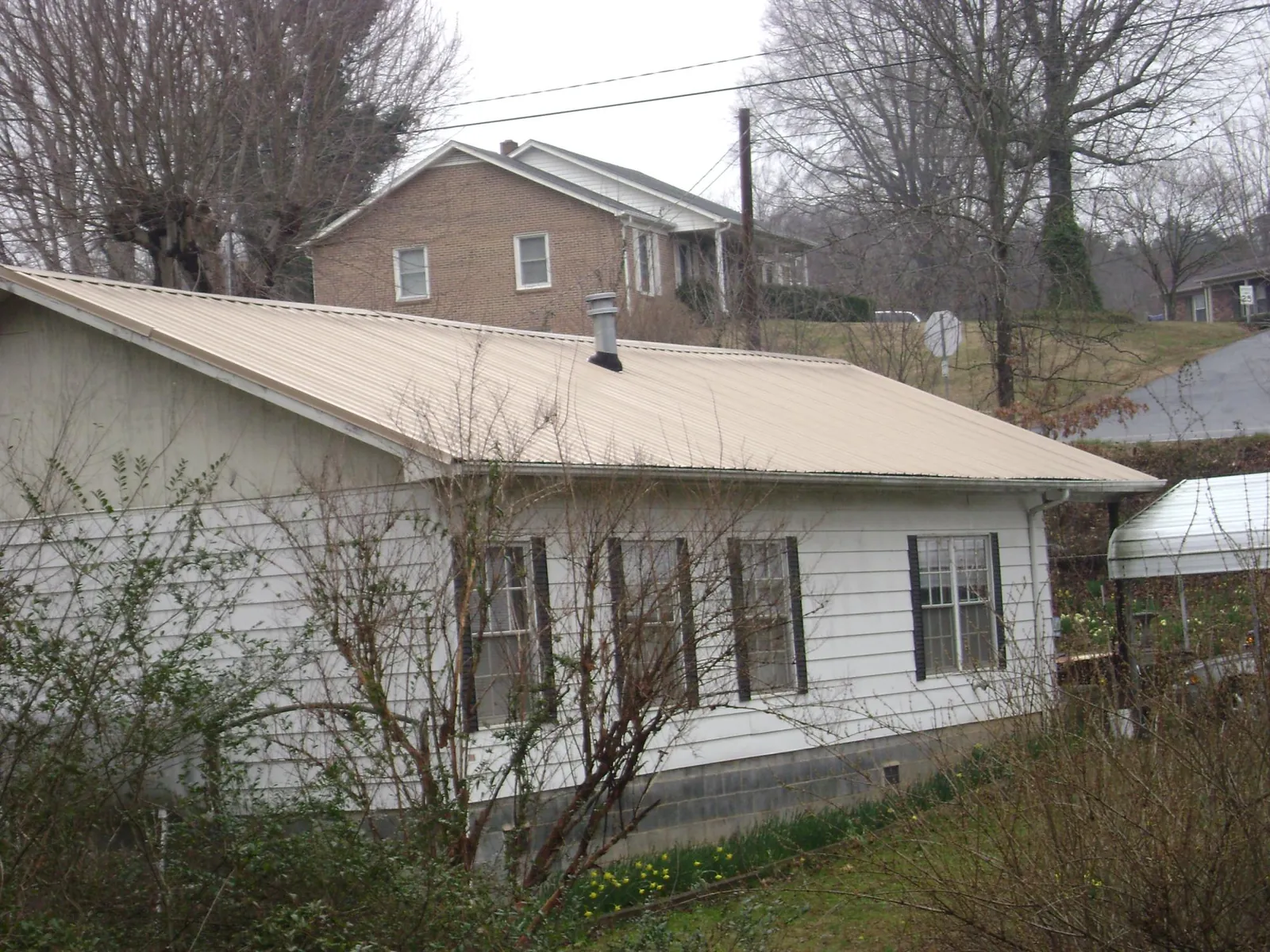 Tan metal roof on a white sided house set into a hillside — Commercial Roofing by Roofing Brothers in East Springfield